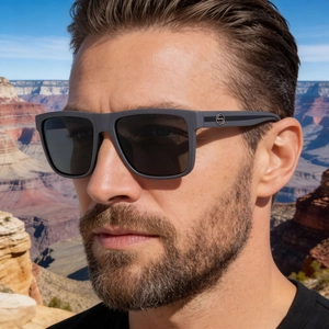 Close-up of matte grey polarized sunglasses worn by a male model in a canyon landscape