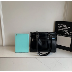 Close-up of black glossy tote bag with metal zipper pocket and marble background