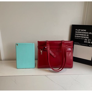 Close-up of red patent leather tote bag with decorative strap and silver zipper detail