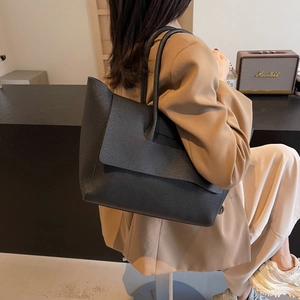 Grand sac cabas en cuir noir grainé avec rabat, porté par un mannequin dans un café
