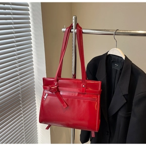Close-up of a large red glossy patent leather shoulder bag with a bow tie strap detail