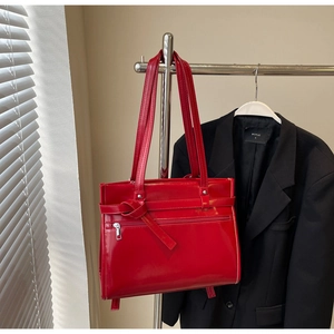 Close-up of bright red patent leather tote bag with knotted belt and front zipper