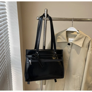 Detail of a black glossy tote bag with knot decor and zipper on a silver hanger
