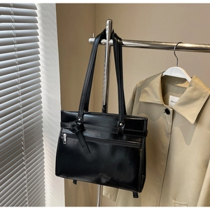 Close-up of a black glossy tote bag with leather knot detail and zipper pocket for women