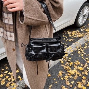 Glossy black underarm bag with bow ribbons and pockets shown in a street style view