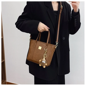Detail of vintage brown tote bag with gold metal plaque and fuzzy cartoon charm accessory