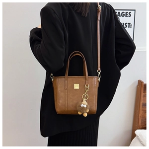 Rear view of a model wearing the brown leather tote bag with a plush monster charm