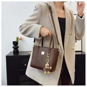 Detailed view of brown PU bucket bag featuring a square metal plate and plush bear charm