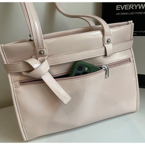 Close-up of glossy pink leather tote bag with stylish knotted strap and front zipper pocket