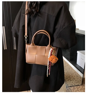 Détail du sac seau en cuir tressé marron avec charme de chien en peluche et sangle