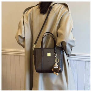 Detail of dark brown tote bag with plush charm and golden hardware on trench coat model