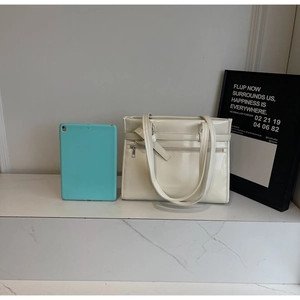 Detail of a creamy white glossy tote bag featuring a knotted strap design and front zipper pocket