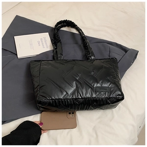 Detail of black quilted tote bag with pleated handles on a grey suit and white background