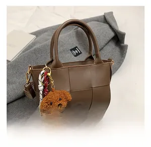 Détail d'un sac sous le bras en cuir tressé marron avec pendentif chien en peluche doux