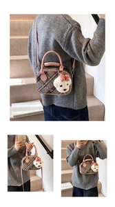 Détail d'un sac Boston à carreaux marron avec anses roses et charm d'ours en peluche