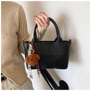 Gros plan d'un sac cabas noir en cuir tressé avec un charmant pendentif ours brun