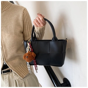 Détail du sac bandoulière tressé noir avec un pendentif ours en peluche marron