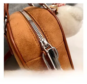 Détail du sac bowling en daim marron avec fermeture éclair argentée et pompon blanc