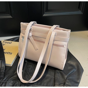 Detail of light pink faux leather tote bag with front zipper on black leather background