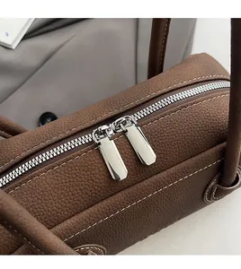 Detail of smooth double metal zippers on brown lychee grain leather bag with white stitching