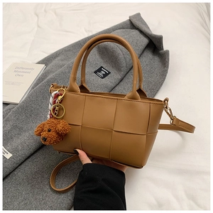 Détail d'un sac à bandoulière tressé marron avec breloque ours en peluche sur tissu doux