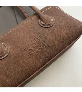 Close-up of brown litchi grain leather bag with white contrast stitching and embossed logo