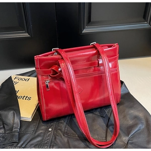 Detail of red glossy leather tote bag with silver zipper and front pocket on dark surface