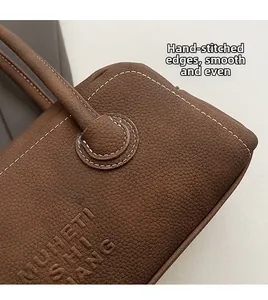 Detail of hand-stitched white contrast seams on brown lychee pattern leather bag