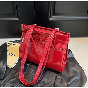 Detail of red patent leather tote bag with silver zipper and decorative belt strap