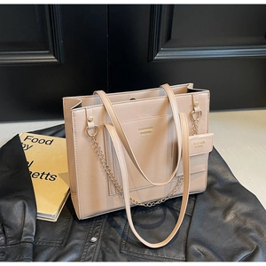 Macro detail of beige matte leather tote bag with gold logo and mini charm on black leather