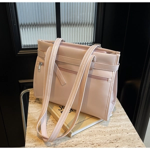 Detail of light pink faux leather tote bag with dual zipper pockets on stone surface