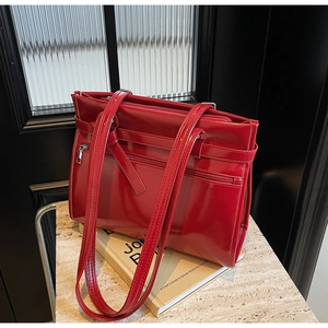 Detail of red patent leather tote bag with decorative buckles and front zipper pocket