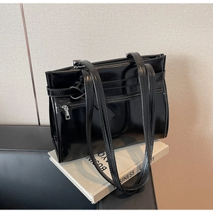 Close-up of glossy black leather tote bag with decorative zipper and buckle details