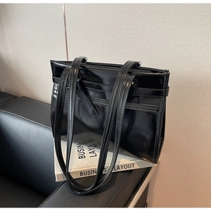 Detail of glossy black leather tote bag with unique multi-strap design and front zip pocket