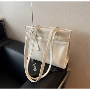 Detail view of cream leather tote bag featuring functional zipper pocket and long shoulder straps