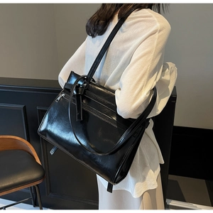 Detail view of a black glossy tote bag with decorative belts on a model for work