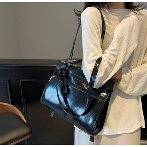 Detail shot of a black glossy leather tote bag featuring functional zippers and belt buckles