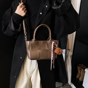Sac sous le bras en cuir tressé marron avec breloque ours porté par un mannequin