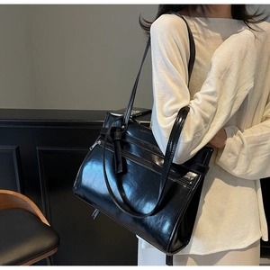 Detail of a black glossy tote bag with dual zippers and smooth patent leather finish