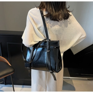 Close-up of glossy black tote bag with dual straps and metallic adjustment buckles