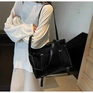 Detail shot of a black glossy leather tote bag showing large capacity and silver buckles