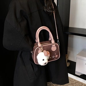 Sac Boston marron avec poignées roses et breloque en peluche sur manteau noir