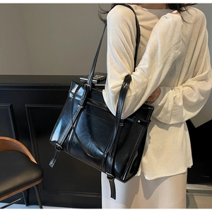 Detail of glossy black tote bag with silver metal buckle on a model for daily commute