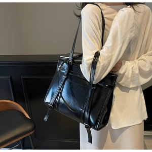 Detail of black glossy tote bag featuring adjustable silver buckle straps and sleek PU leather