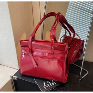 Detail of red glossy tote bag featuring decorative belt straps and functional front zipper