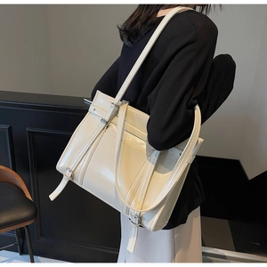 Detail of a creamy beige tote bag with glossy leather finish and decorative straps