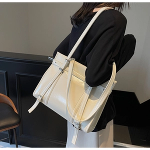 Detail of a large cream leather tote bag with silver buckle straps and glossy finish