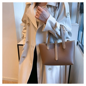 Detail of a brown lychee pattern leather bucket bag held by a model in a white coat