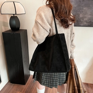 Große schwarze Tragetasche mit Krokodilprägung am Modell in minimalistischer Umgebung