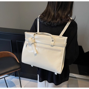 Cream-colored stylish backpack with top handle and decorative knot strap shown on model